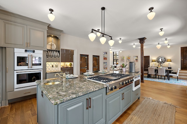 kitchen featuring white appliances, a sink, gray cabinets, dark stone countertops, and a center island with sink