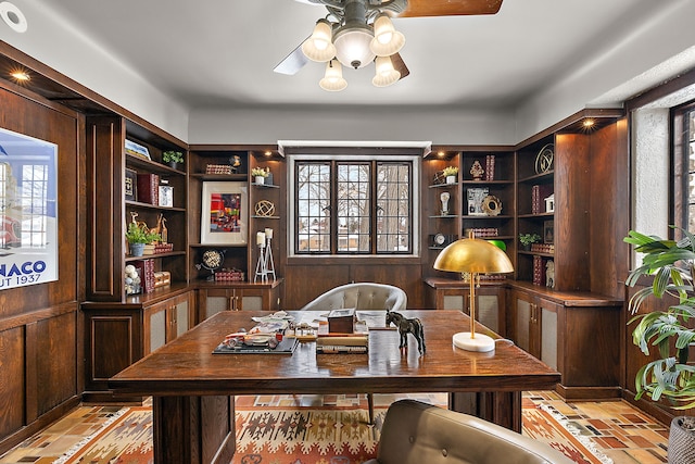 office area featuring ceiling fan, wood walls, and brick floor