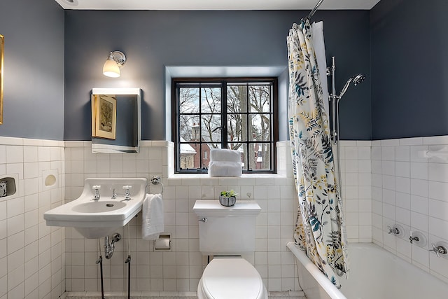 bathroom with toilet, shower / tub combo, tile walls, and wainscoting