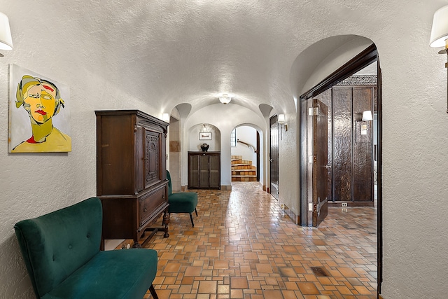 hall featuring arched walkways, a textured wall, lofted ceiling, stairway, and a textured ceiling