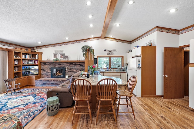 dining space with vaulted ceiling with beams, a textured ceiling, a fireplace, ornamental molding, and light wood-type flooring