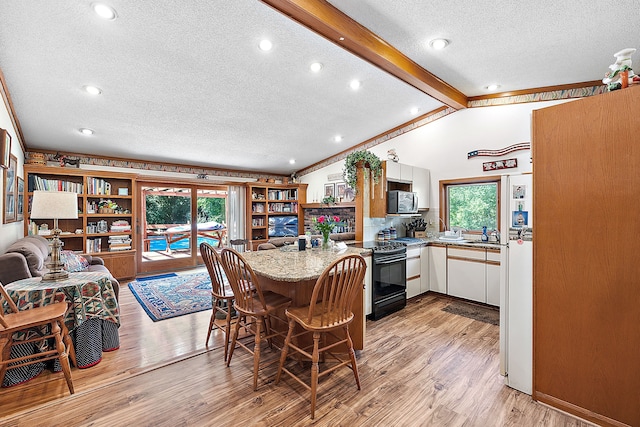 dining space featuring plenty of natural light, vaulted ceiling with beams, and light wood-style flooring