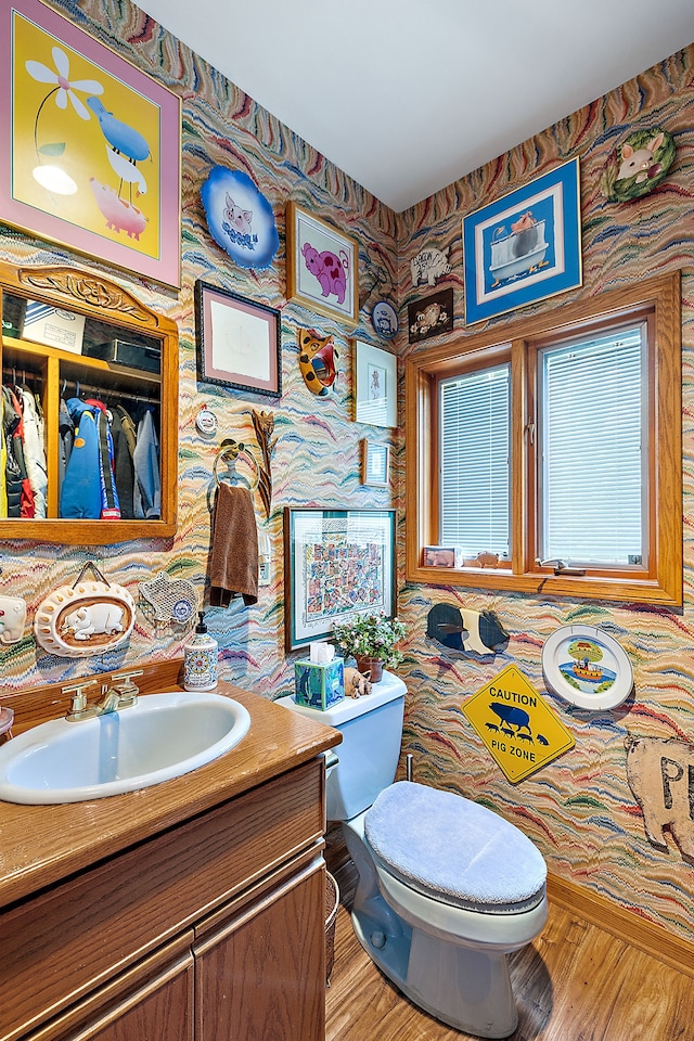 bathroom with toilet, wallpapered walls, wood finished floors, and vanity