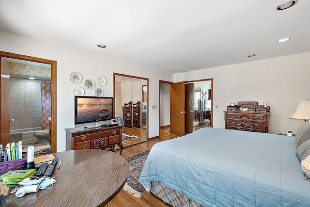 bedroom featuring ensuite bathroom, recessed lighting, wood finished floors, and multiple closets