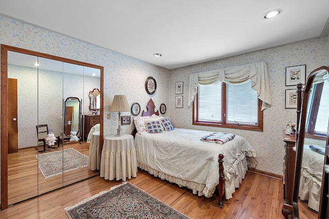 bedroom with wallpapered walls, wood-type flooring, baseboards, and a closet