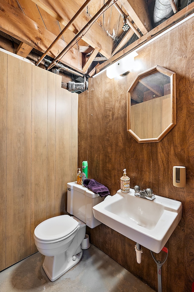 half bathroom with concrete flooring, a sink, toilet, and wooden walls