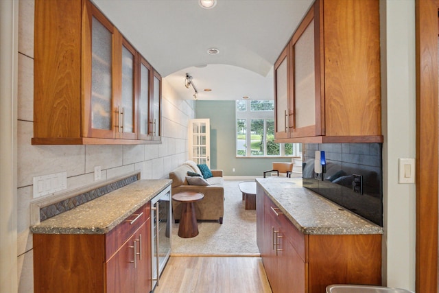 kitchen featuring lofted ceiling, light wood-type flooring, light stone countertops, and wine cooler