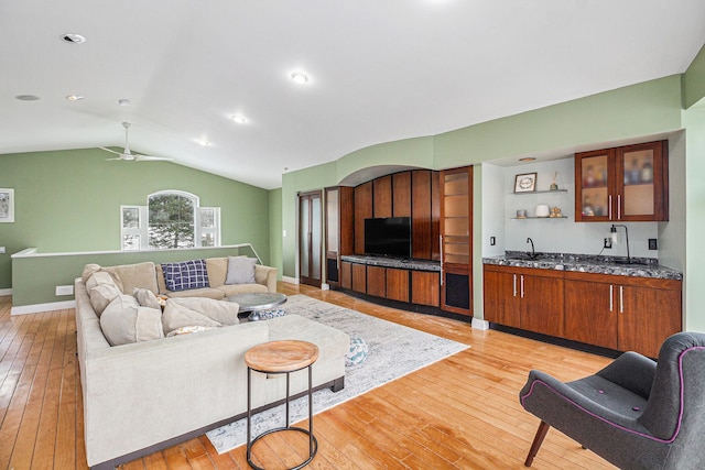 living room featuring ceiling fan, light hardwood / wood-style flooring, sink, and vaulted ceiling