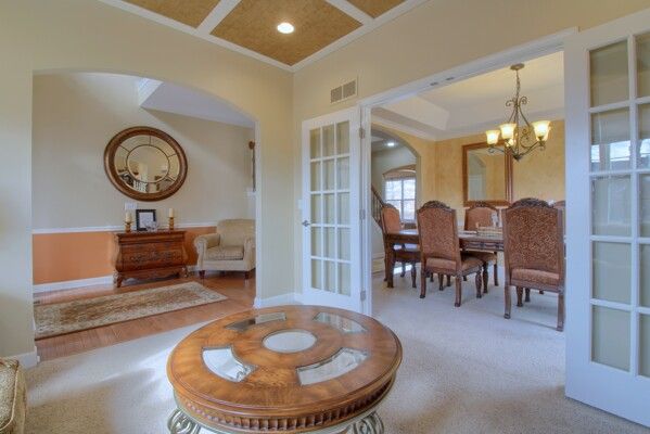 living area with crown molding, coffered ceiling, visible vents, french doors, and an inviting chandelier