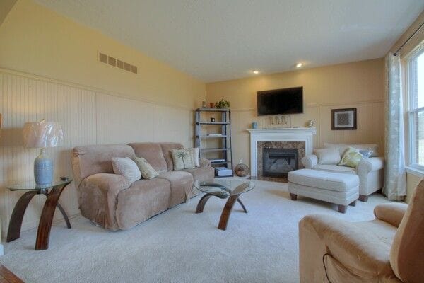 living room featuring carpet floors, a fireplace, visible vents, and a decorative wall