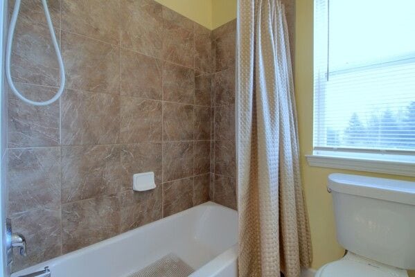 full bath featuring toilet and shower / tub combo with curtain