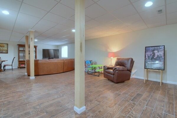 basement featuring visible vents, wood finished floors, a paneled ceiling, and baseboards