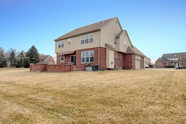 rear view of property featuring an attached garage, brick siding, central AC unit, and a yard