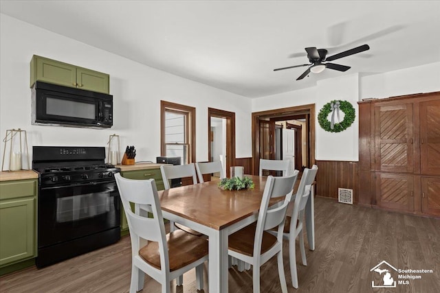 dining space with ceiling fan, wooden walls, and dark hardwood / wood-style flooring