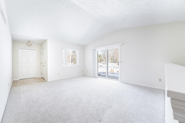 interior space with a textured ceiling, vaulted ceiling, baseboards, and light colored carpet