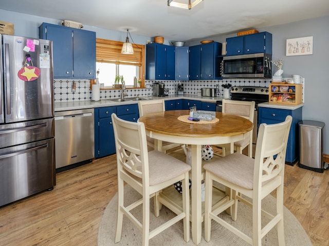 kitchen featuring appliances with stainless steel finishes, tasteful backsplash, blue cabinets, light hardwood / wood-style floors, and sink