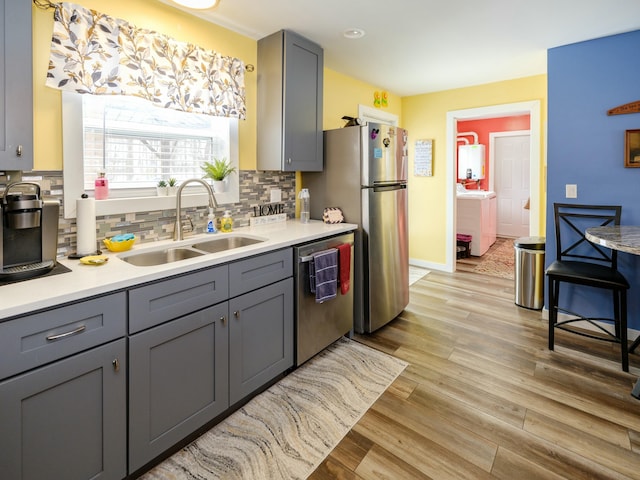 kitchen with appliances with stainless steel finishes, light hardwood / wood-style flooring, tasteful backsplash, gray cabinetry, and sink