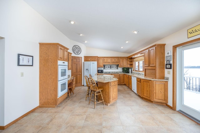 kitchen with lofted ceiling, a center island, sink, white appliances, and a kitchen bar