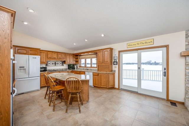 kitchen featuring light tile patterned floors, a breakfast bar area, white appliances, lofted ceiling, and a kitchen island