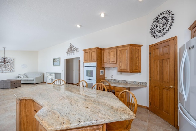 kitchen featuring a kitchen island, stainless steel refrigerator, light stone countertops, white double oven, and a breakfast bar area