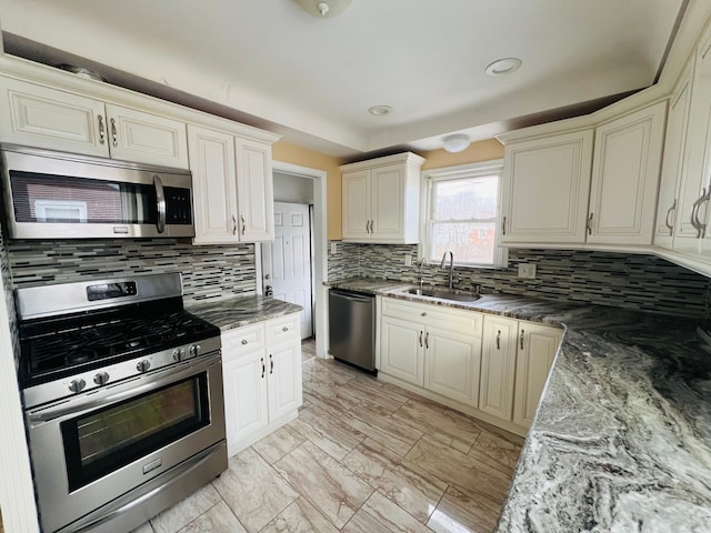 kitchen featuring dark stone countertops, appliances with stainless steel finishes, cream cabinetry, and a sink