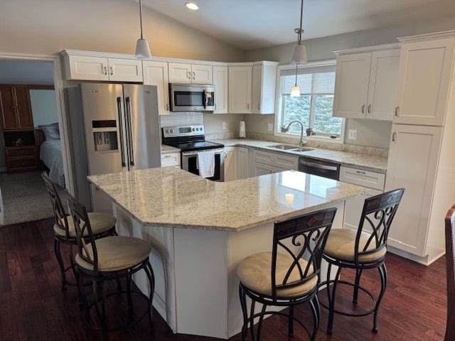 kitchen with appliances with stainless steel finishes, a kitchen island, sink, and white cabinetry