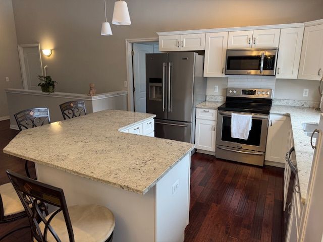 kitchen featuring appliances with stainless steel finishes, a breakfast bar, a center island, white cabinetry, and decorative light fixtures