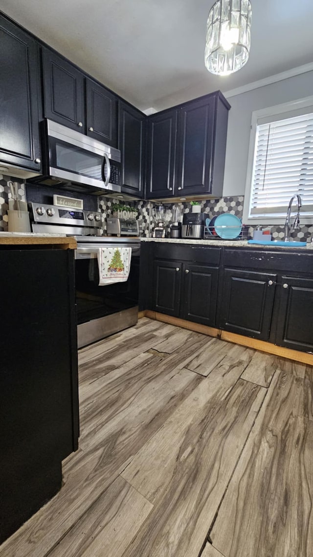 kitchen with light hardwood / wood-style floors, crown molding, stainless steel appliances, and decorative backsplash