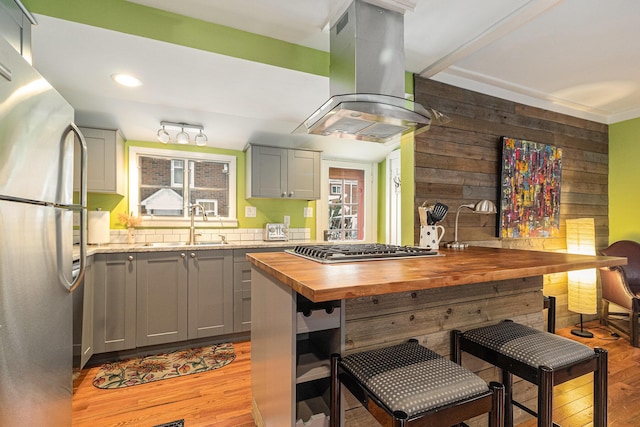 kitchen featuring sink, island exhaust hood, gray cabinetry, stainless steel appliances, and butcher block countertops