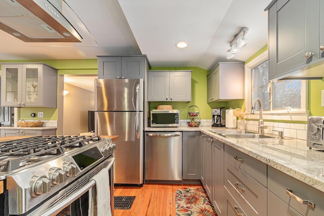 kitchen with sink, stainless steel appliances, light stone countertops, and light hardwood / wood-style floors