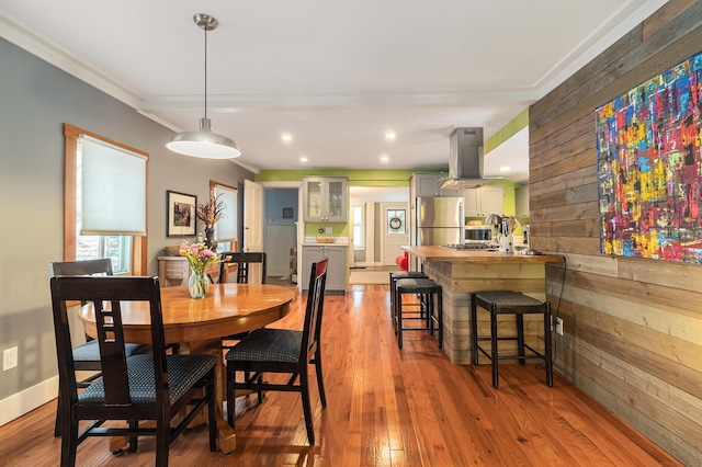 dining room with light hardwood / wood-style floors, wooden walls, and ornamental molding