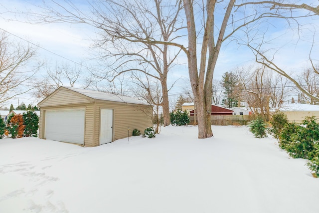 yard covered in snow featuring a garage, fence, and an outbuilding