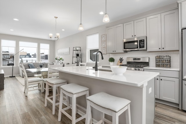 kitchen featuring a center island with sink, appliances with stainless steel finishes, light countertops, and decorative light fixtures