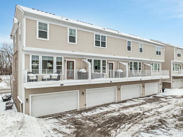 snow covered rear of property featuring an attached garage and a balcony