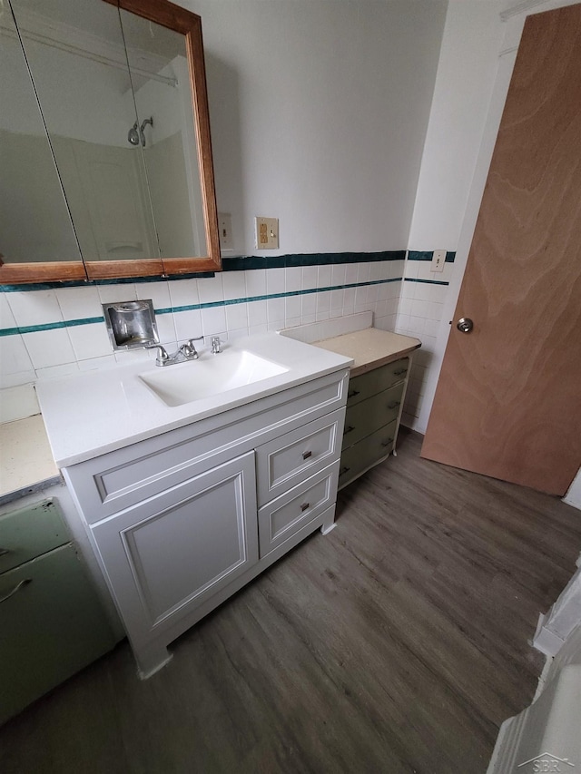 bathroom featuring a wainscoted wall, wood finished floors, walk in shower, vanity, and tile walls