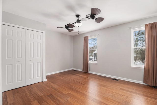 unfurnished bedroom with multiple windows, a closet, ceiling fan, and wood-type flooring