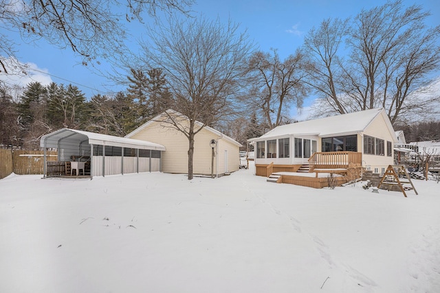 snow covered rear of property with a deck, a carport, and a sunroom