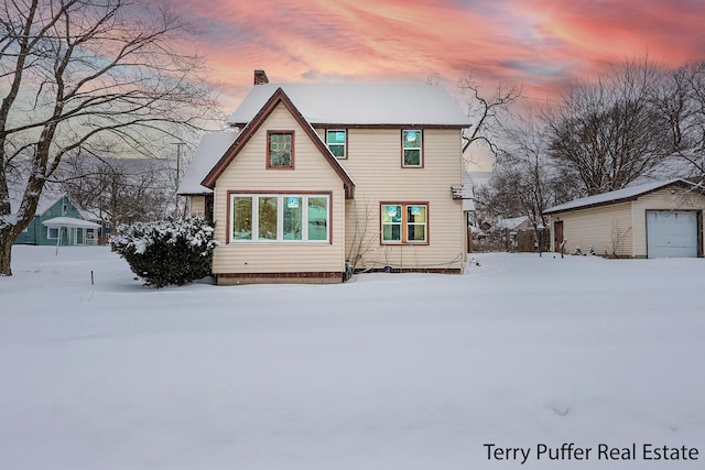 snow covered rear of property with an outbuilding, a chimney, and a garage