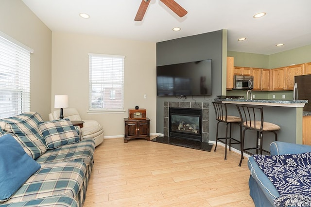 living room with ceiling fan, plenty of natural light, light wood-type flooring, and a tiled fireplace