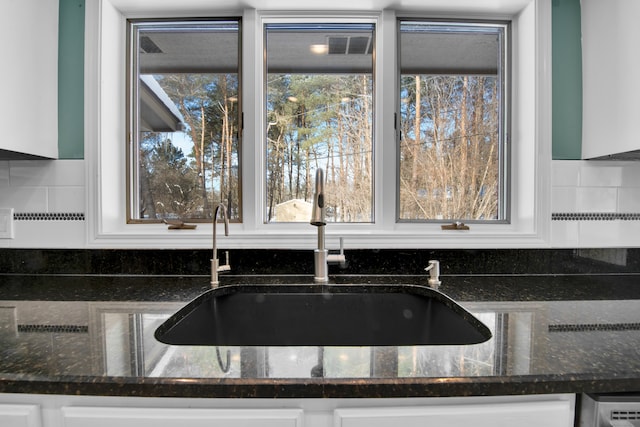 kitchen featuring dark stone counters, a healthy amount of sunlight, a sink, and white cabinets