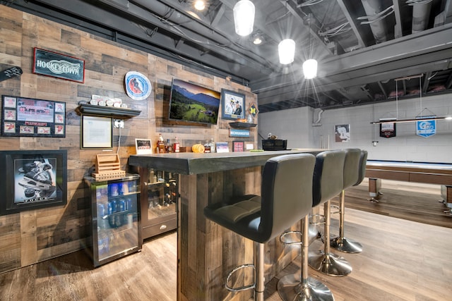 bar featuring light wood finished floors, a bar, and concrete block wall