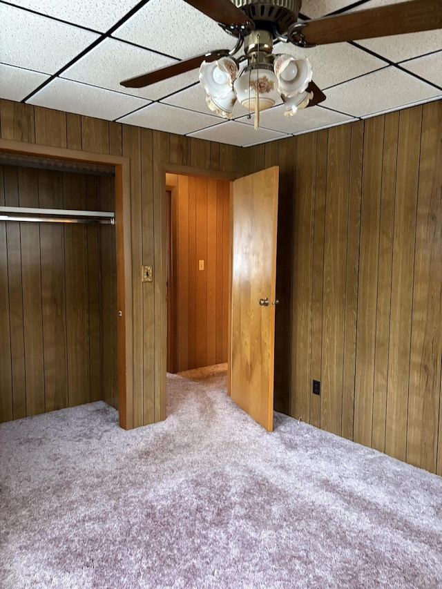 unfurnished bedroom featuring ceiling fan, a closet, wooden walls, and carpet flooring