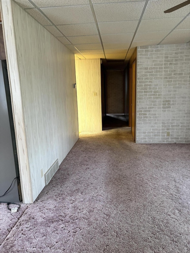 empty room with brick wall, wooden walls, a paneled ceiling, and carpet floors