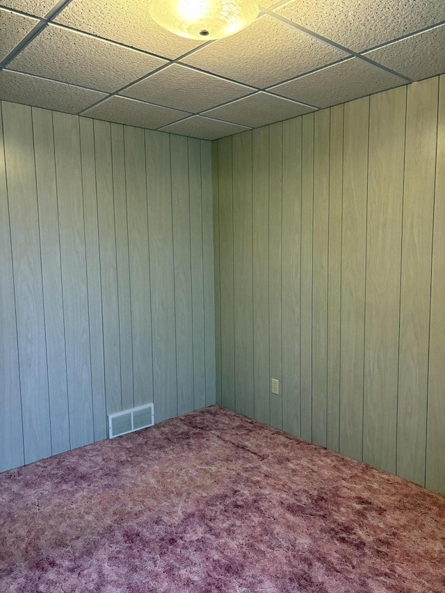 carpeted spare room featuring wooden walls and a paneled ceiling