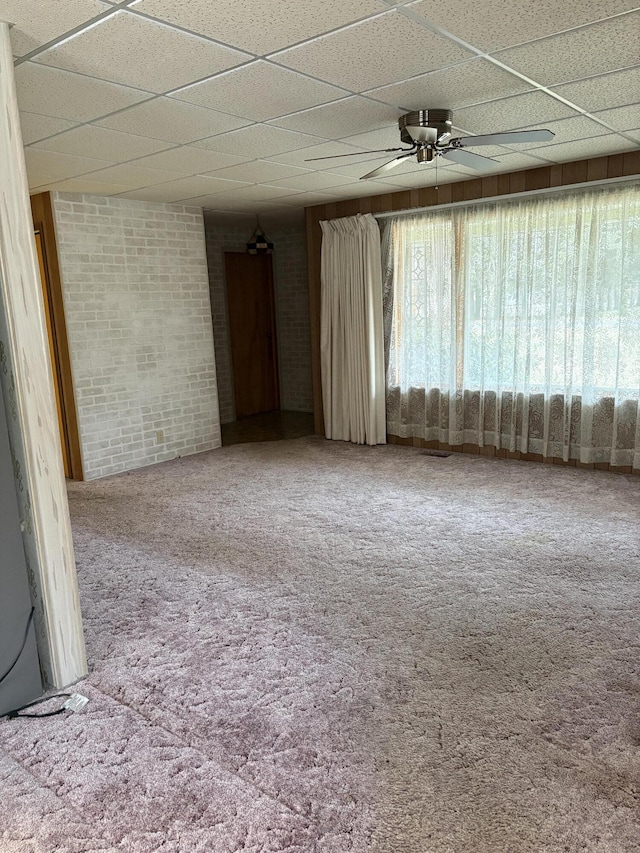 empty room with brick wall, carpet flooring, ceiling fan, and a drop ceiling