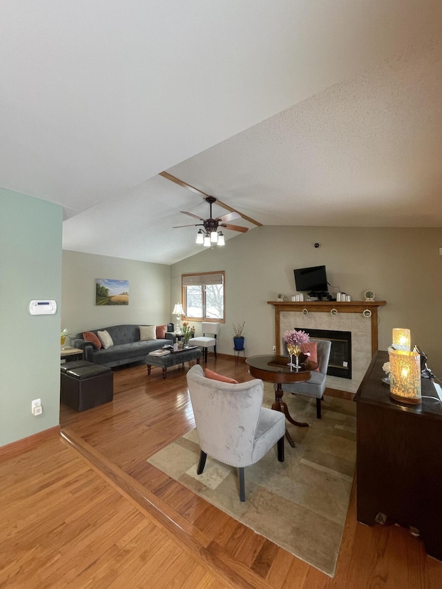 living room with a tiled fireplace, ceiling fan, vaulted ceiling, and hardwood / wood-style flooring