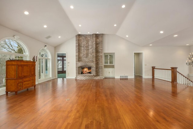 unfurnished living room featuring an inviting chandelier, high vaulted ceiling, wood-type flooring, and a fireplace