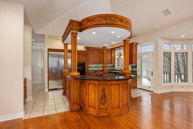 kitchen with backsplash, a center island, light wood-type flooring, stainless steel appliances, and ornate columns