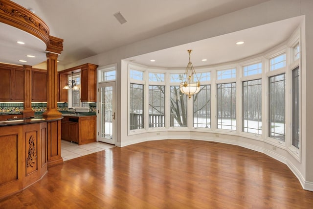 unfurnished dining area with an inviting chandelier, plenty of natural light, and light hardwood / wood-style flooring