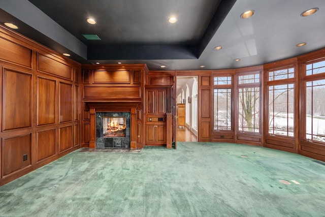 unfurnished living room with a tray ceiling, light carpet, wood walls, and a fireplace